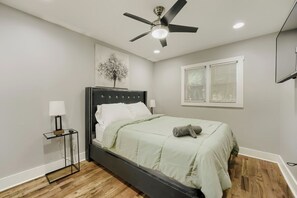 Una camera da letto con un letto, una ventola a soffitto, una finestra con persiane e un'opera d'arte appesa al muro.