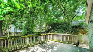 Eine Holzterrasse mit Geländer, umgeben von Bäumen und einem Haus im Hintergrund.
