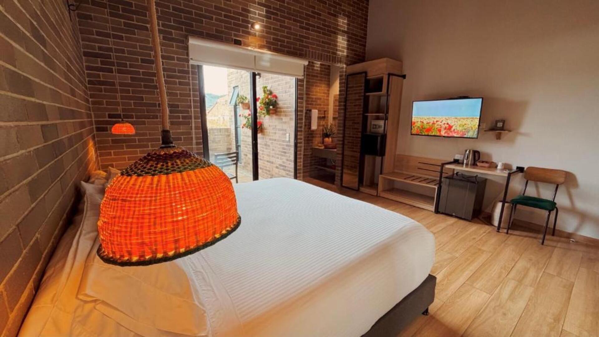Una habitación de hotel moderna con una cama grande, televisor, escritorio pequeño y balcón con vistas.