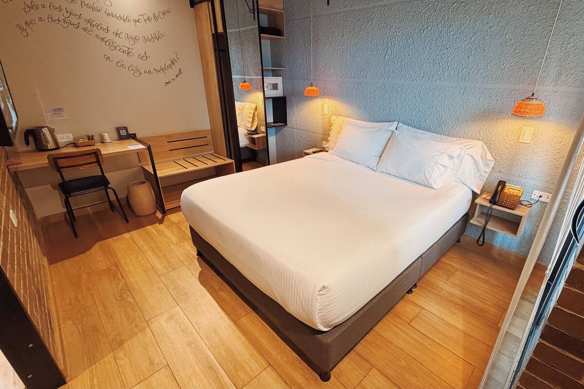 Ein Hotelzimmer mit einem großen Bett, einem Schreibtisch, einem Sessel, einem Telefon und einer Wand mit strukturierter Oberfläche.