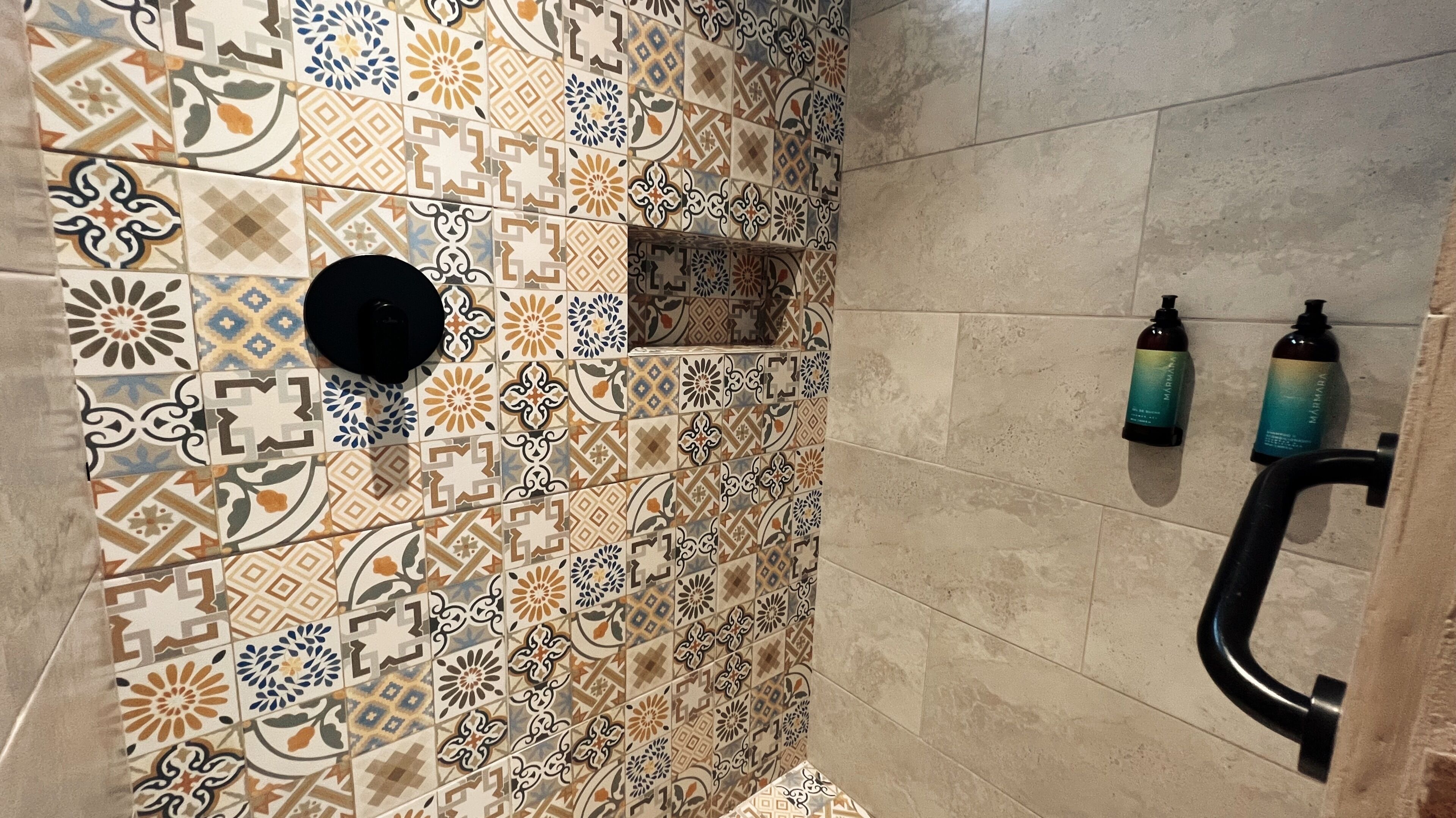 A bathroom with patterned tiles, a black circular object, and two bottles on the wall.