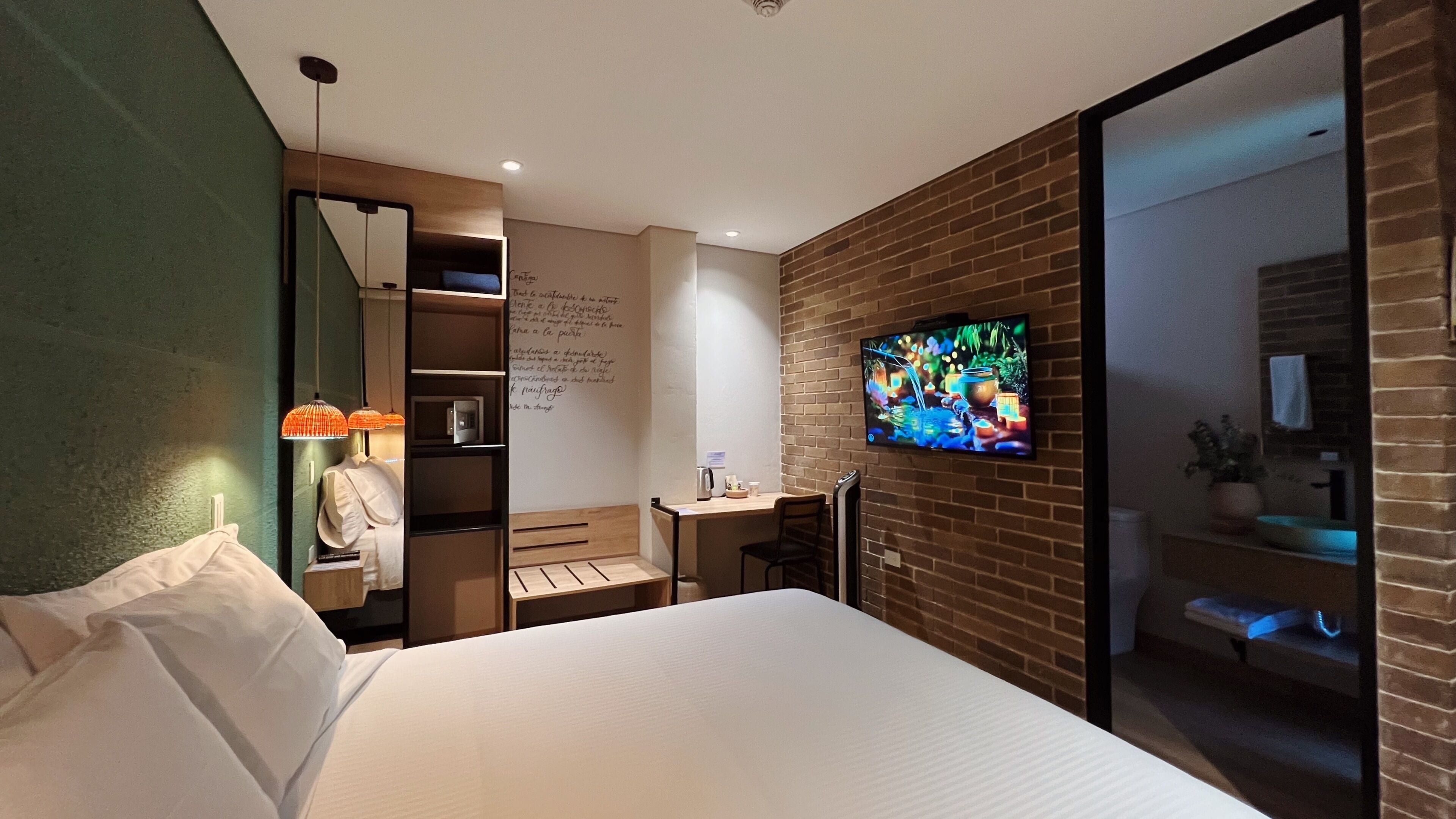 A hotel room with a bed, desk, chair, TV, and a brick wall.