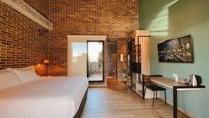 Una habitación de hotel con pared de ladrillo, cama, escritorio con silla y un cuadro en la pared.