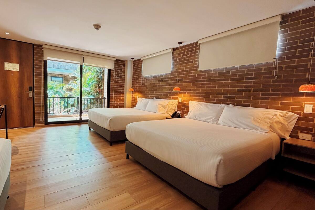 Ein Hotelzimmer mit zwei Betten, einem Balkon, Holzboden und einer Ziegelwand.