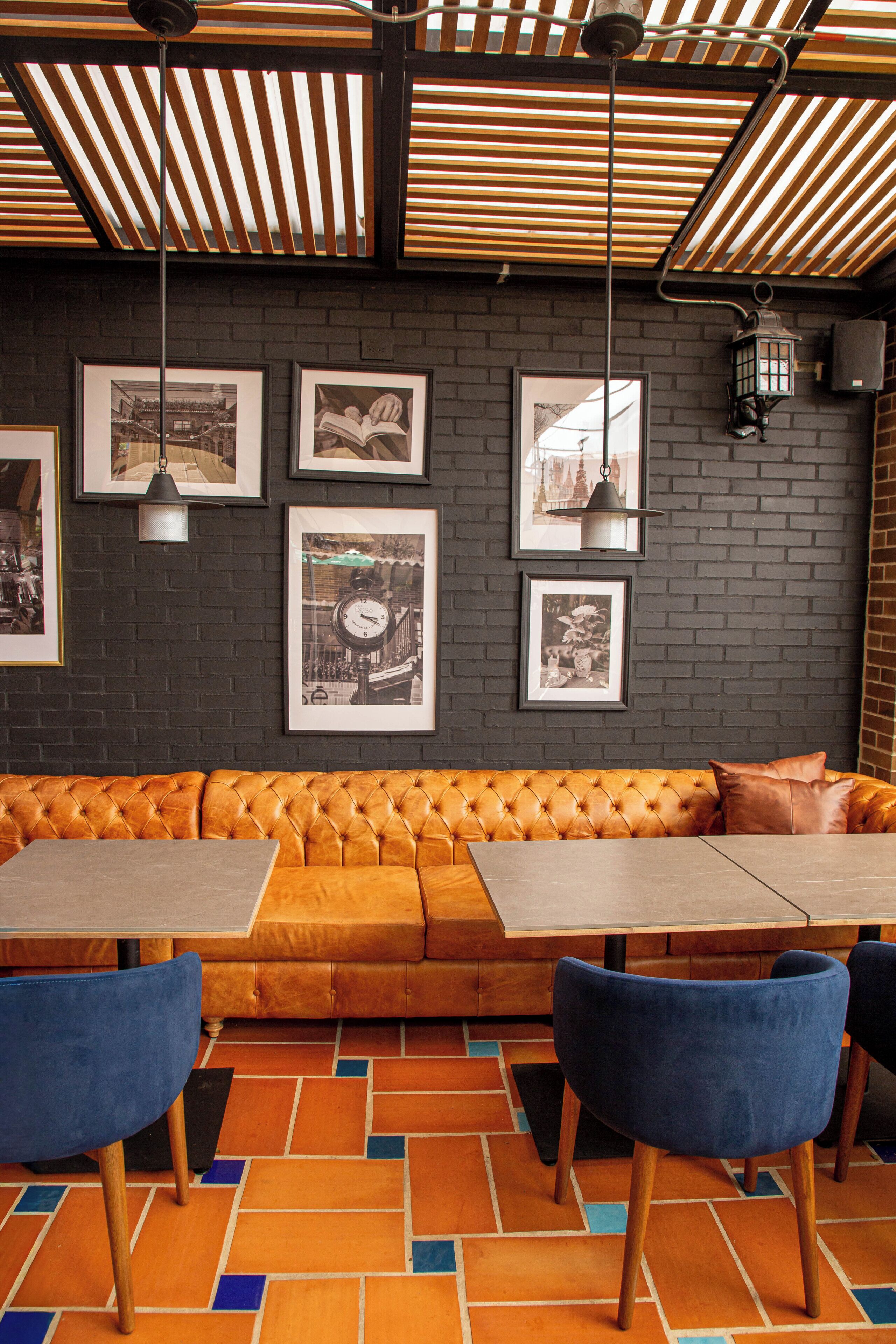 Interior de restaurante con pared de ladrillo, cuadros enmarcados, sofá naranja con capitonado y sillas azules.