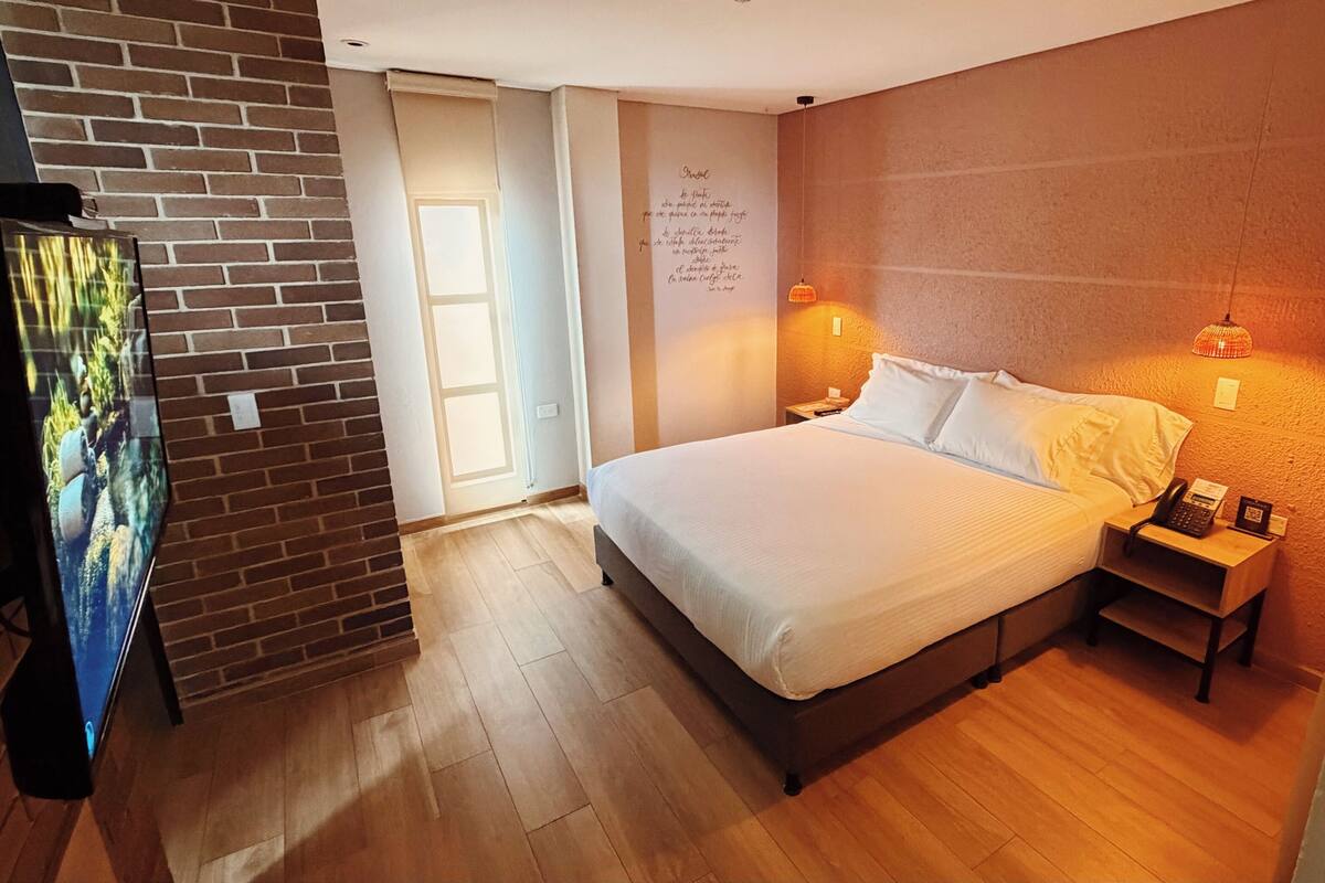 Ein Schlafzimmer mit einem Bett, Holzboden, einer Ziegelwand, einer Tür und einer Wandleuchte.