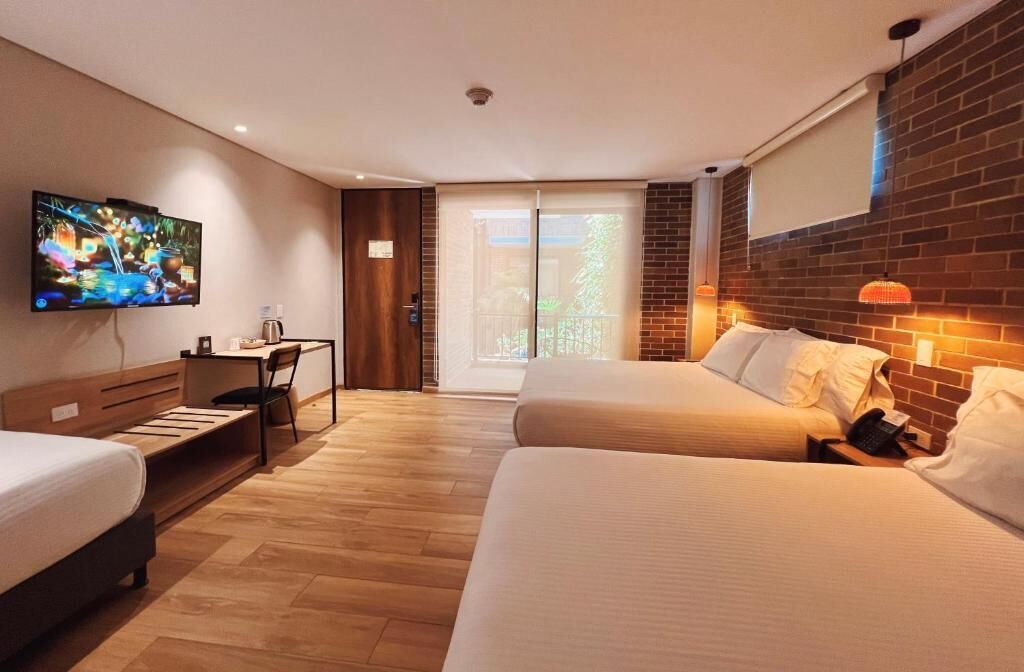 A hotel room with two beds, a desk, a TV, and a sliding glass door to the outside.