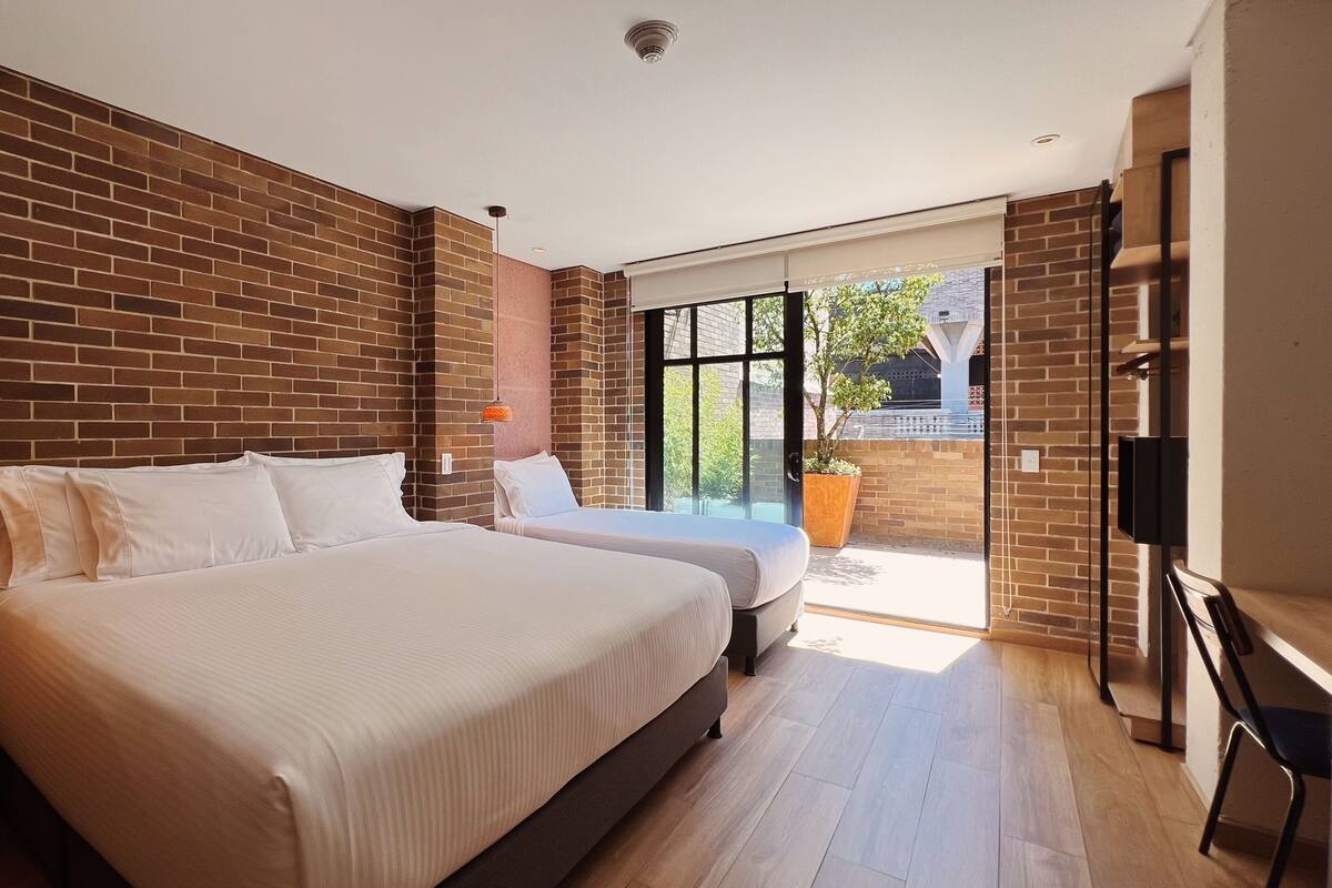 Ein Schlafzimmer mit zwei Betten, einer Ziegelwand, einem großen Fenster und einem Fernseher.