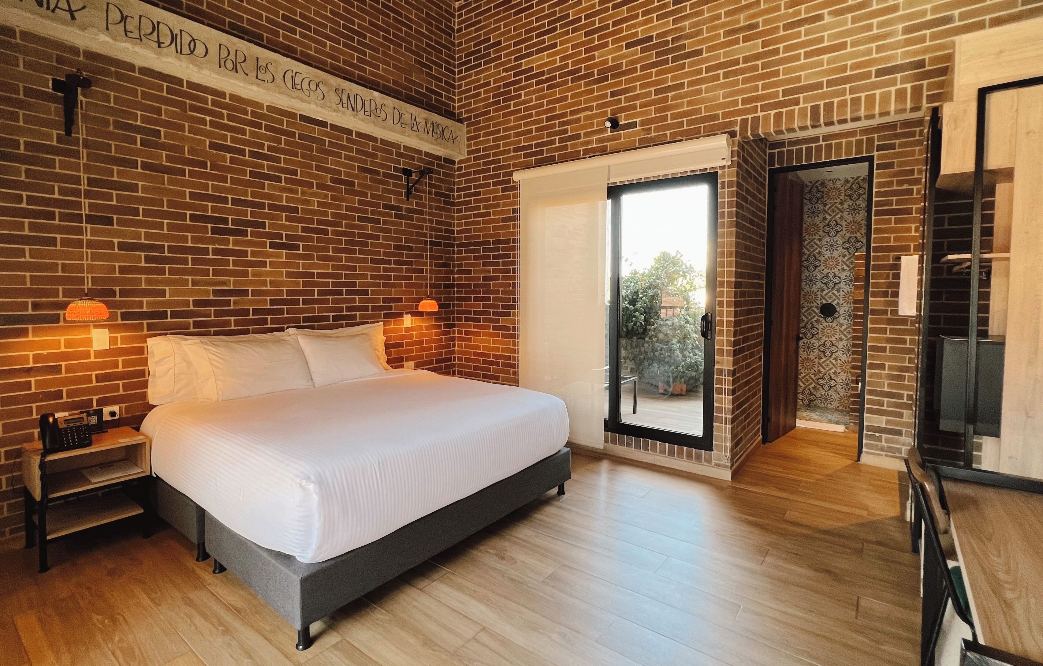 A bedroom with a brick wall, a bed, bedside lamps, a nightstand, and a sliding door to a balcony.