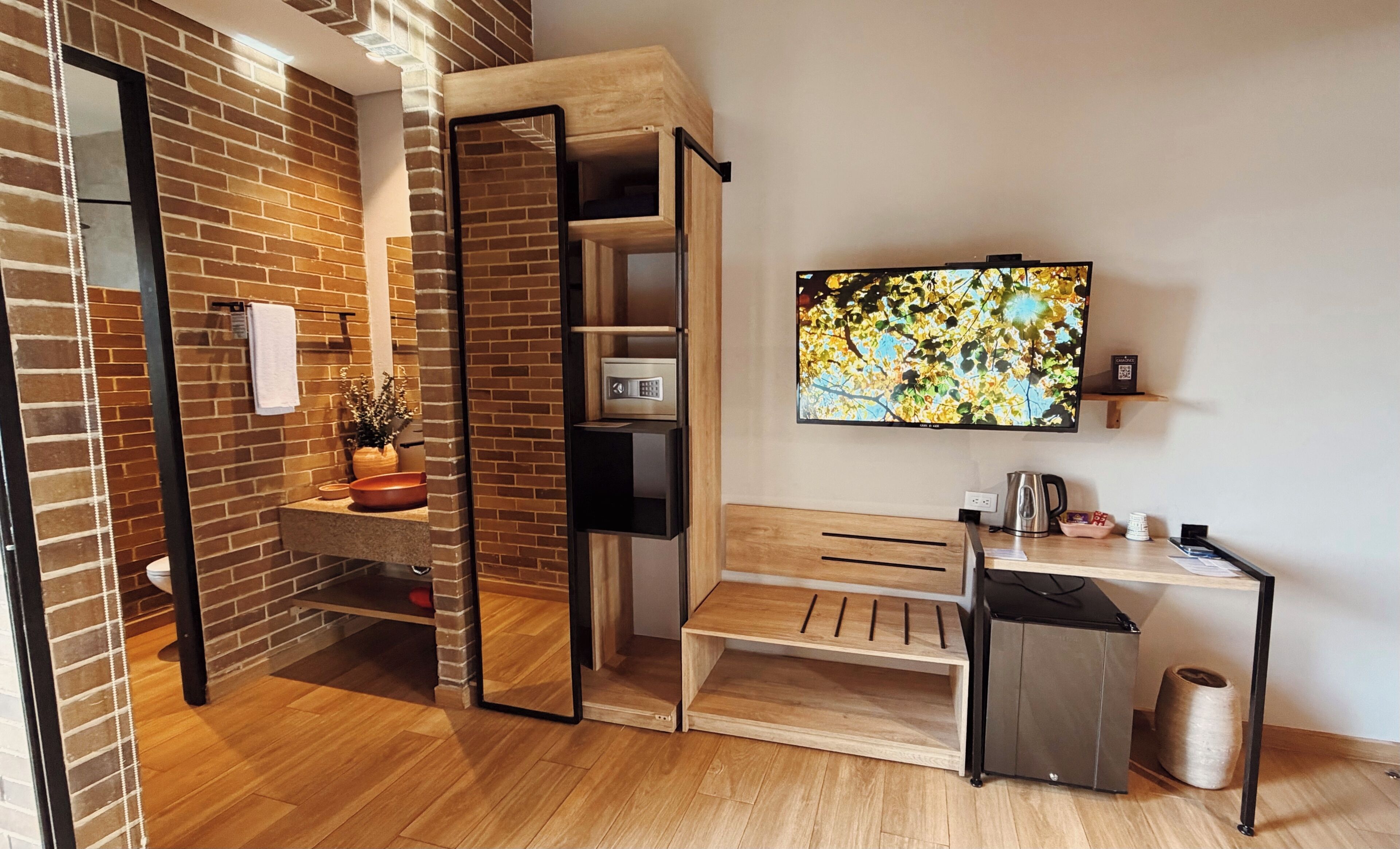A modern bathroom with a wooden bench, a toilet, a sink, a mirror, and a television mounted on the wall.