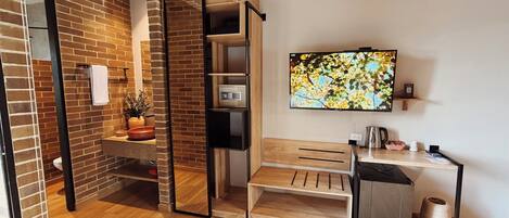 A modern bathroom with a wooden bench, a toilet, a sink, a mirror, and a television mounted on the wall.
