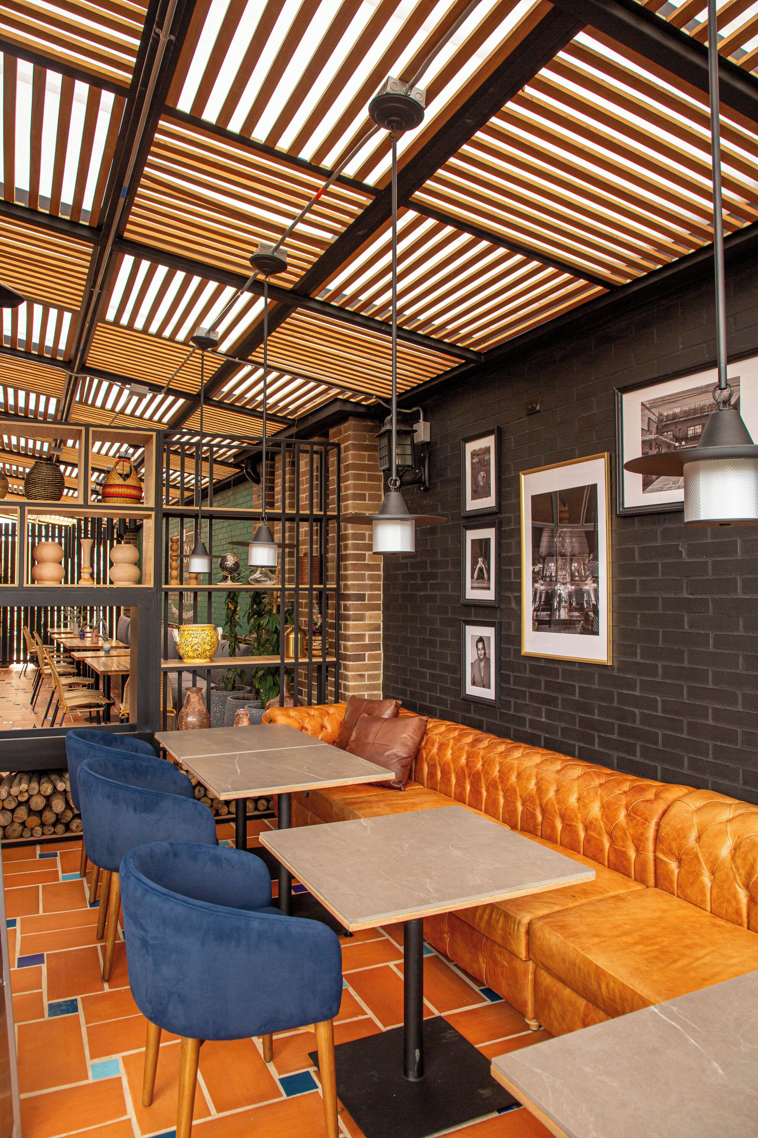 A restaurant interior with wooden slatted ceilings, tables, blue chairs, and a leather booth.