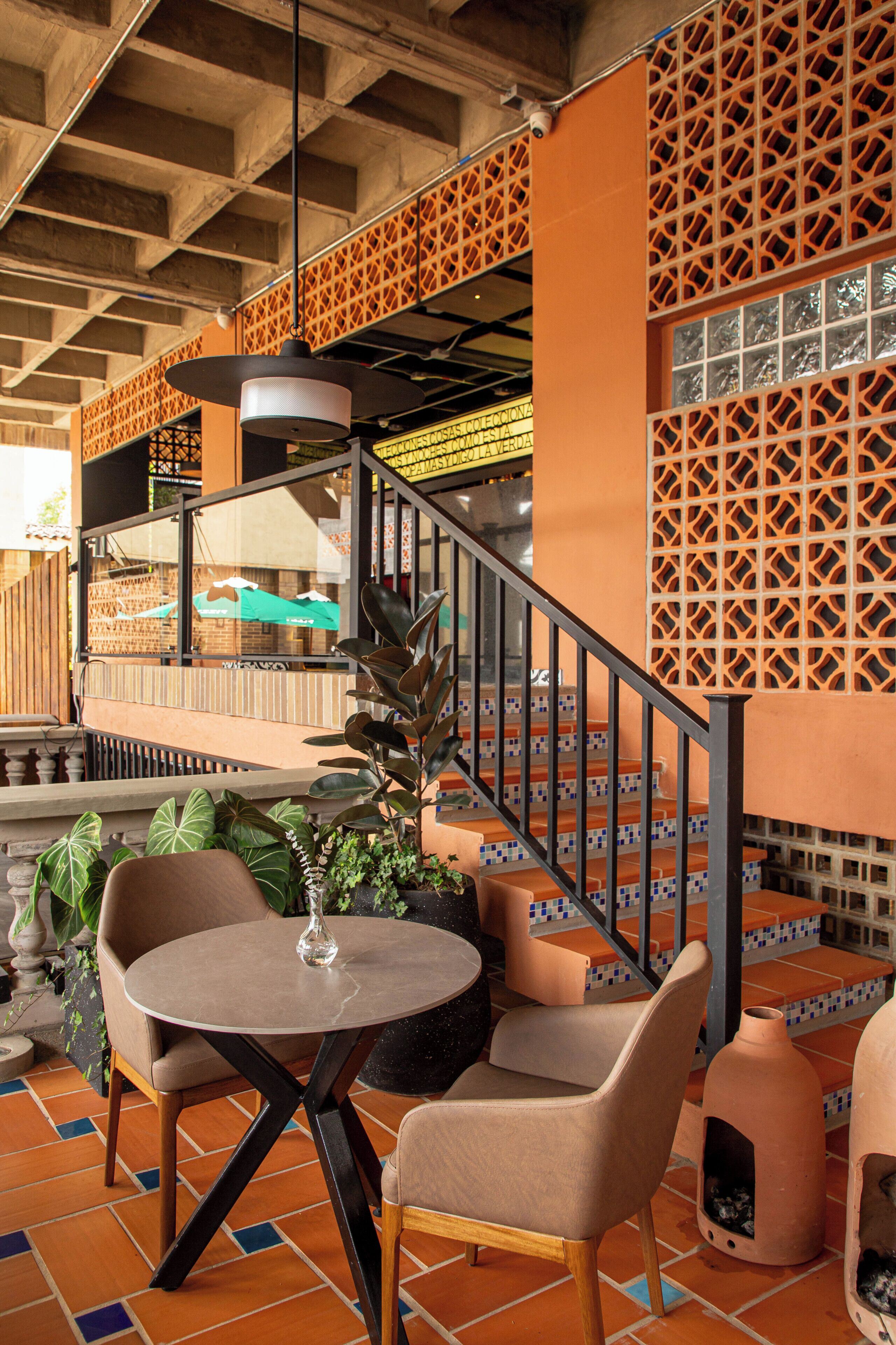 A terrace with a round table and two chairs, a staircase with orange and blue tiles, and a view of the street.