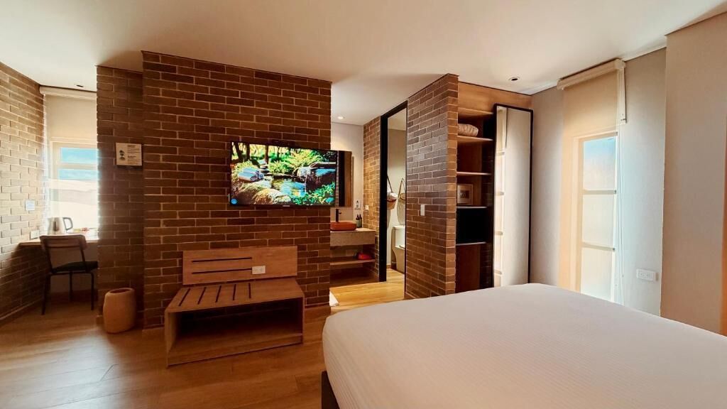 Ein Schlafzimmer mit einem Bett, einem an einer Ziegelwand montierten Fernseher, einer Holzbank und einem Kleiderschrank.
