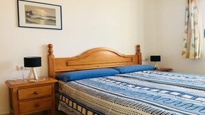 Et soveværelse med en træseng, et natbord, en lampe, et billede i ramme på væggen og et vindue med gardiner.