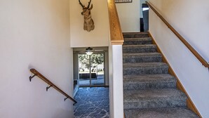 Una escalera con barandilla de madera y peldaños alfombrados que conduce a una habitación con una cabeza de venado montada en la pared.