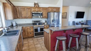 Una cocina con armarios de madera, electrodomésticos de acero inoxidable, encimera de granito y una zona de bar con taburetes.