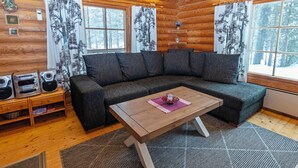 L’intérieur d’une cabane en rondins, avec un canapé d’angle, une table basse en bois et une cheminée.