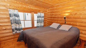 Une chambre dans un chalet en rondins, avec un lit, des rideaux et une table de chevet.