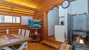 L’intérieur chaleureux d’un chalet avec une table à manger en bois, des chaises, un téléviseur, une cheminée et une horloge au mur.