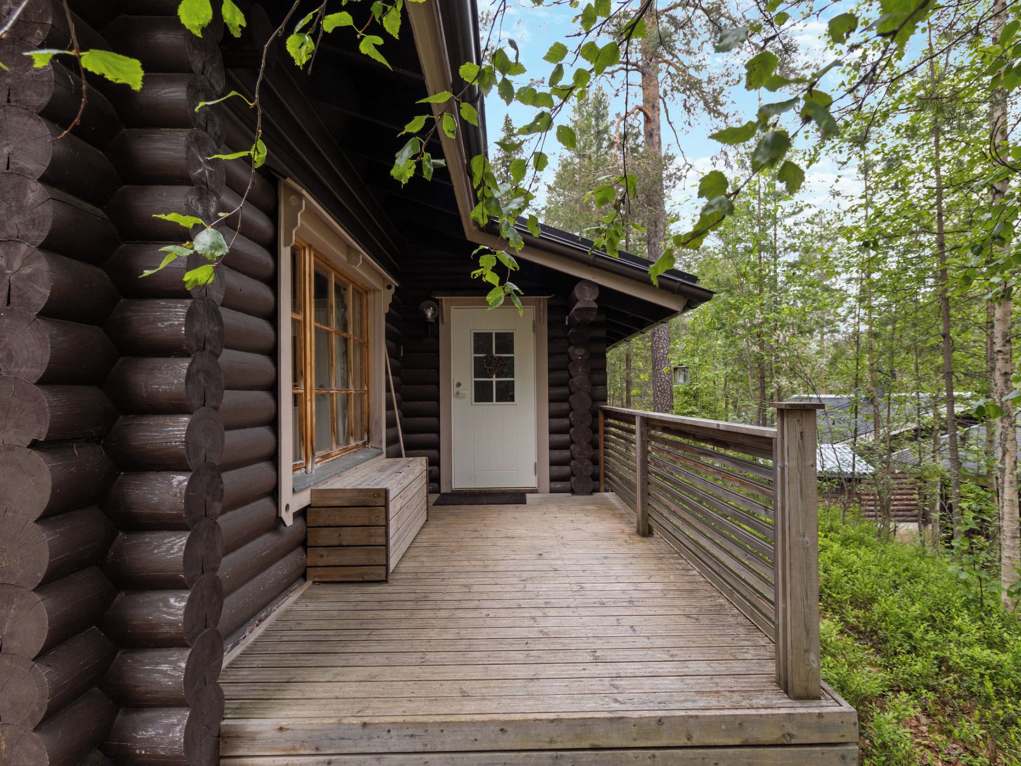 A log cabin with a wooden deck, a front door, and a window.
