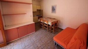 A compact room with a kitchenette, a dining table with chairs, and a single bed. - Lorenza by Interhome (Rosolina Mare)