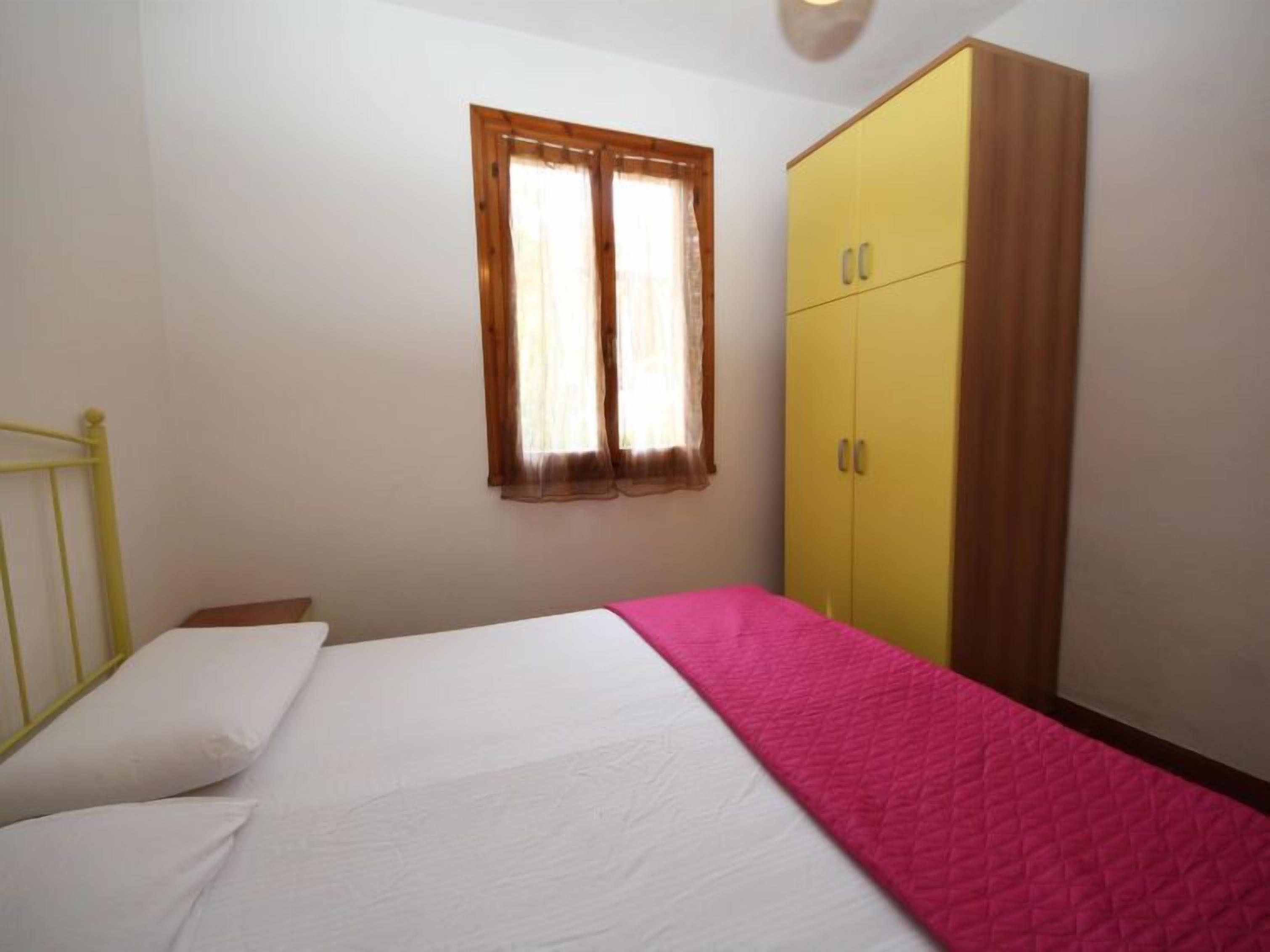 A bedroom with a bed, a window with curtains, and a yellow wardrobe.