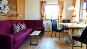 A cozy living room with a purple sofa, a wooden coffee table, and a dining area with a wooden table and chairs. - Three-room vacation apartment 2, approx. 63 sqm with balcony and wonderful view (Reit im Winkl)