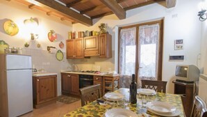 A kitchen with wooden cabinets, a refrigerator, a dining table with a sunflower tablecloth, and a television. - "La dolce collina" by Interhome (Castiglione del Lago)