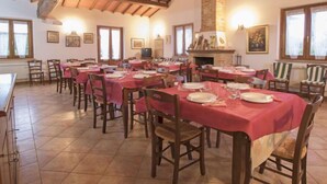 A dining hall with multiple tables set for meals, wooden chairs, a brick fireplace, and framed artwork on the walls. - "La dolce collina" by Interhome (Castiglione del Lago)