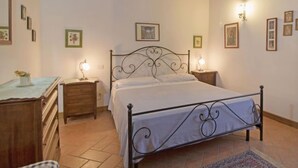 A bedroom with a metal bed frame, wooden dresser, bedside tables with lamps, and framed pictures on the walls. - Villastrada by Interhome (Castiglione del Lago)