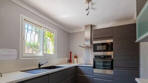 A modern kitchen with dark cabinetry, a stainless steel range hood, a built-in microwave, and a double sink. - Cascabelle by Interhome (Sainte Maxime)