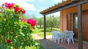 Un patio con mesa y sillas, rodeado por un jardín con plantas en flor.