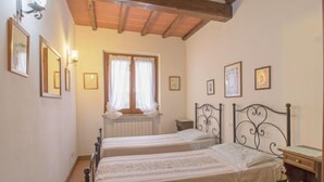 Un dormitorio con dos camas individuales, techo de madera, ventana con cortinas e imágenes enmarcadas en las paredes.