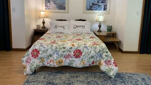 A neatly arranged bedroom with a floral bedspread, two bedside lamps, and two framed pictures on the wall. - View Peaceful Pond while lounging in this open studio apartment! (Warsaw)