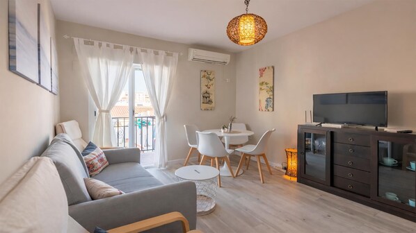 A modern living room with a sofa, dining table, chairs, a TV, and artwork on the walls.