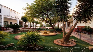 A courtyard with a central fountain, surrounded by well-maintained grass, palm trees, and a variety of plants.