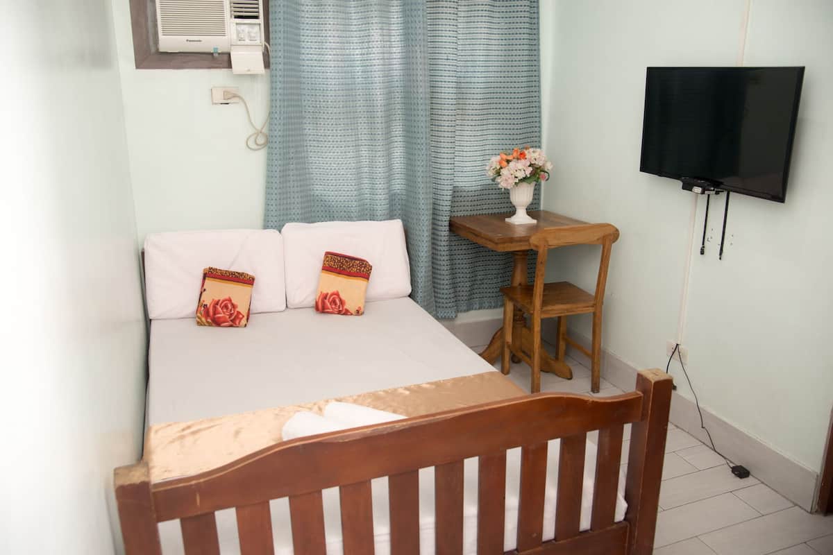 A bedroom with a bed, a wooden nightstand, a TV, and a window with curtains.