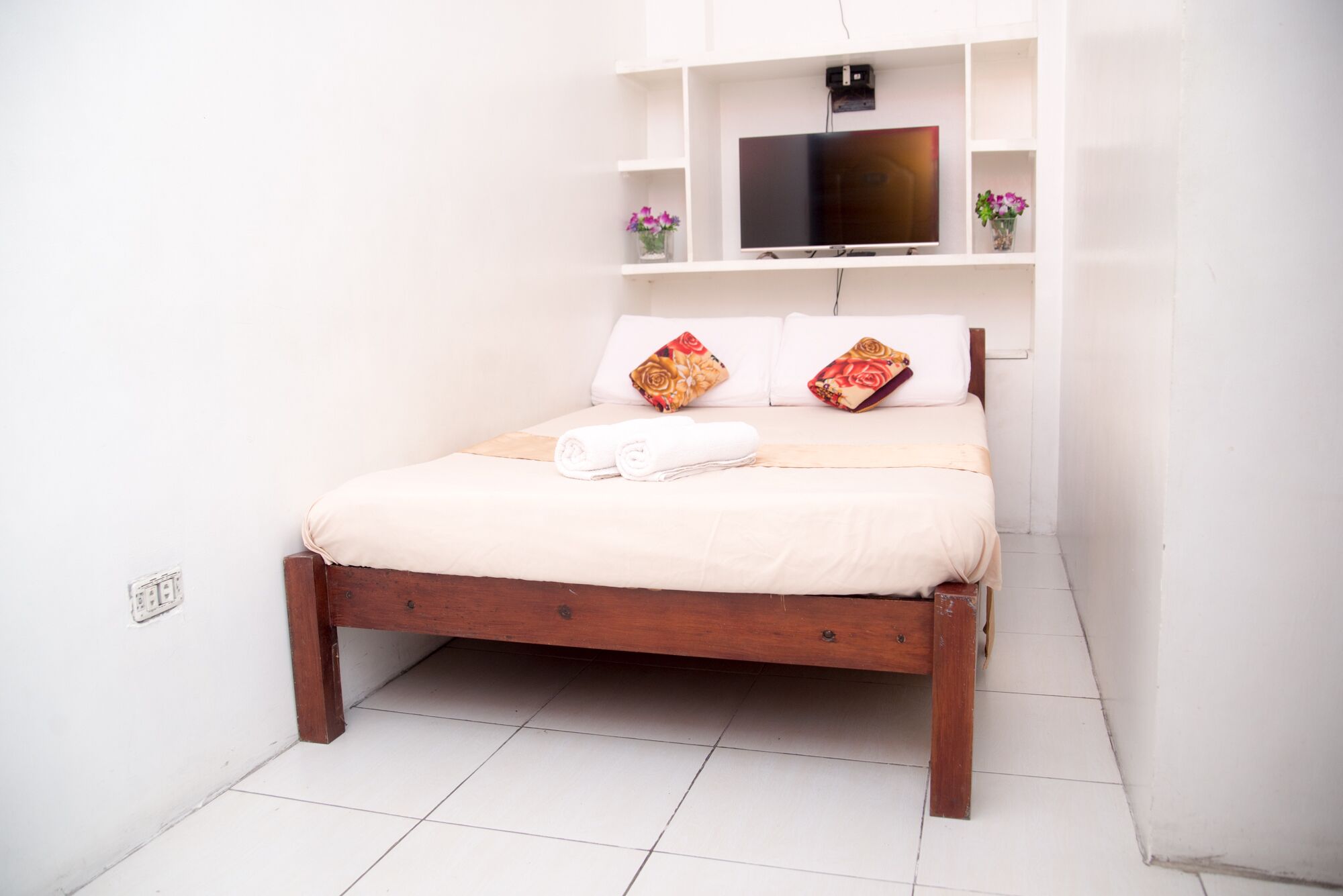 A small, neatly made bed with a wooden frame, white bedding, and two decorative pillows.