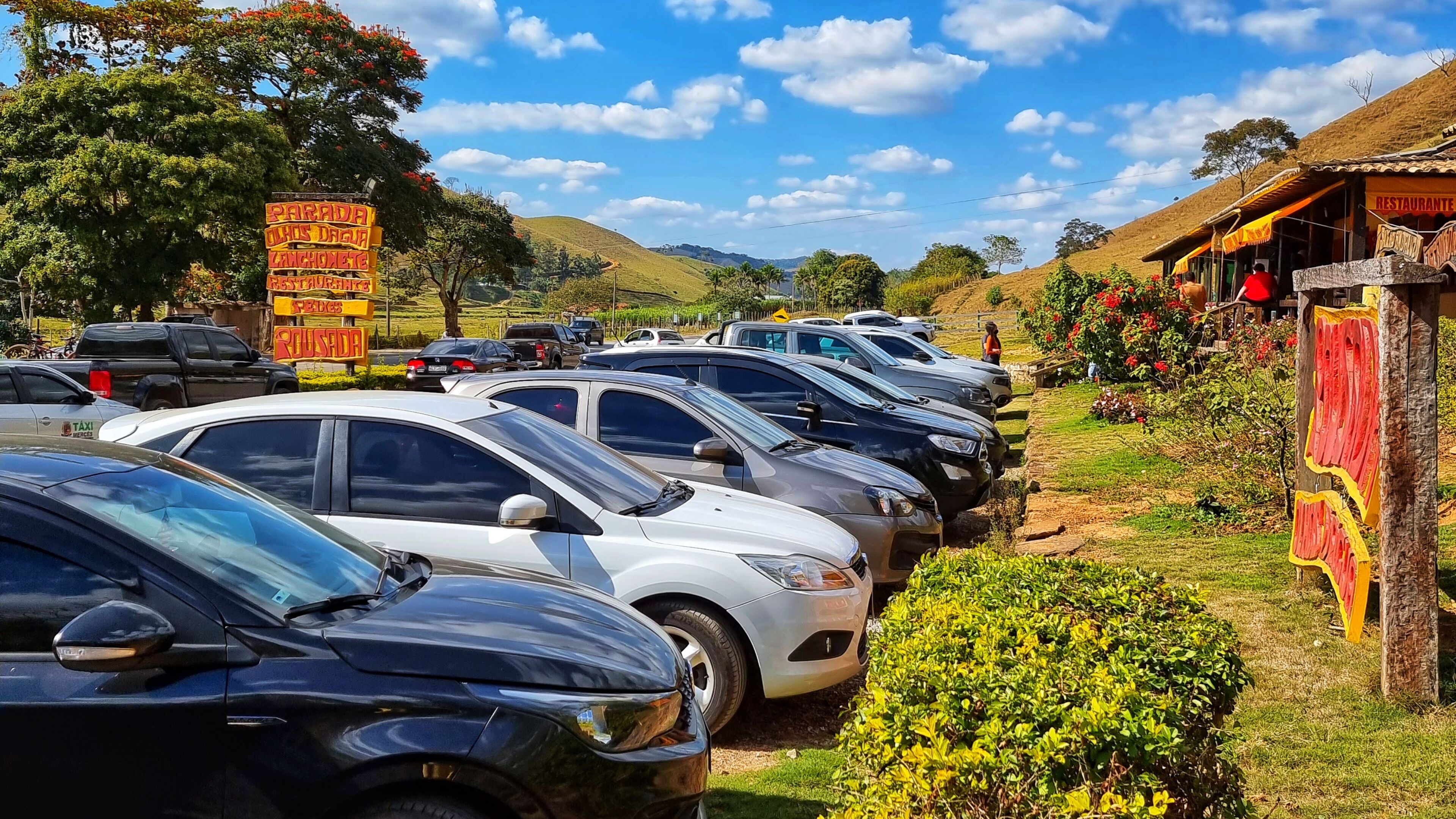 A parking lot with multiple cars parked in rows, a signboard with text, and a building with a sign that reads "RESTAURANTE".