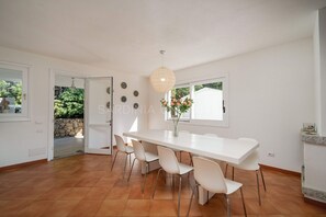 A spacious dining area with a white table and chairs, a hanging light fixture, and a view of the outdoors through a window. - Villa in Santa Teresa Gallura with 3 bedrooms sleeps 8 (Santa Teresa Gallura)