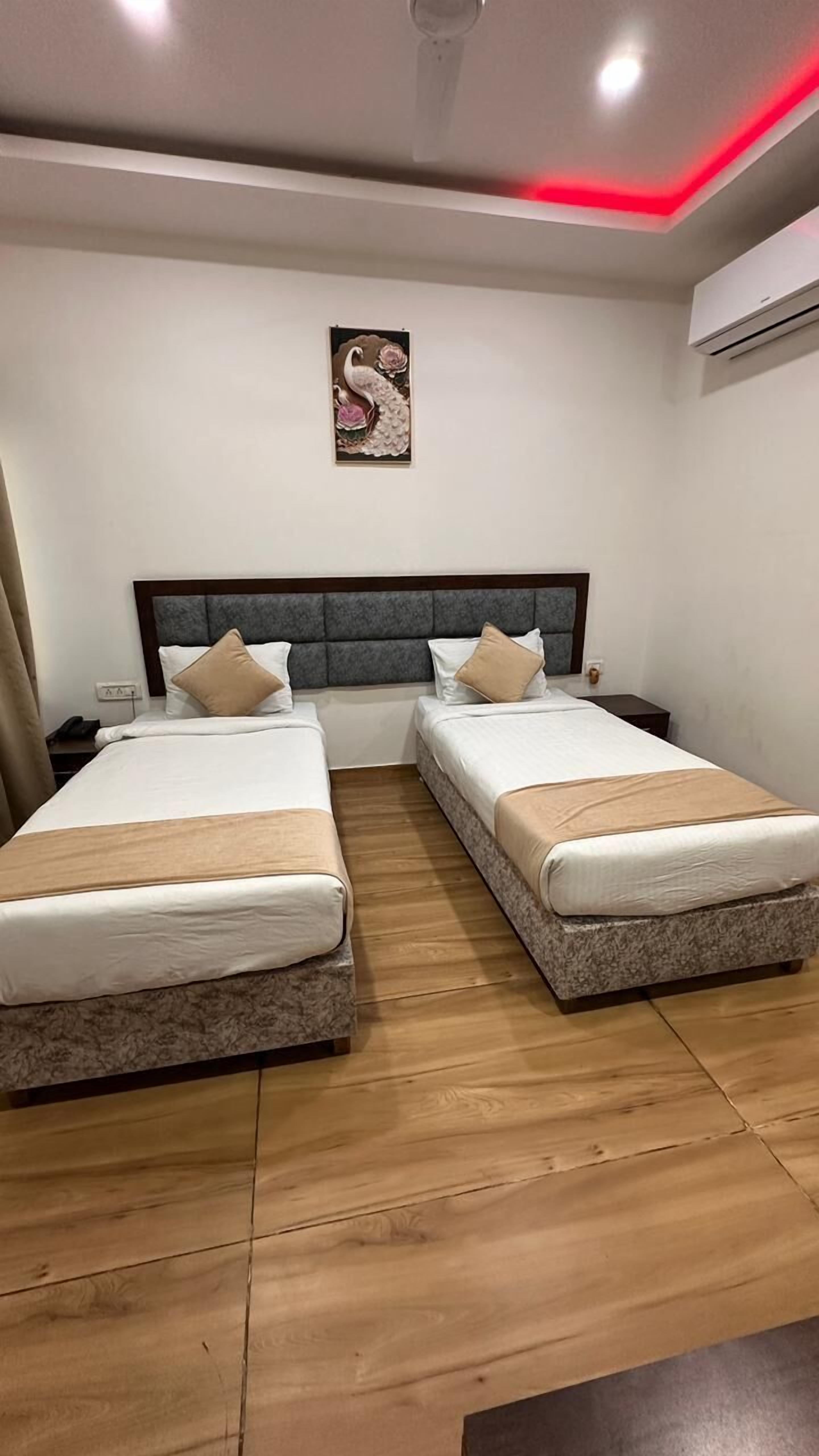 A hotel room with two beds, a grey headboard, a wall-mounted air conditioner, and a painting of swans.