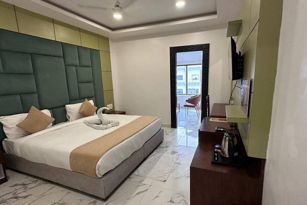 A modern hotel room with a large bed, a green headboard, a flat-screen TV, and a view of the outside.