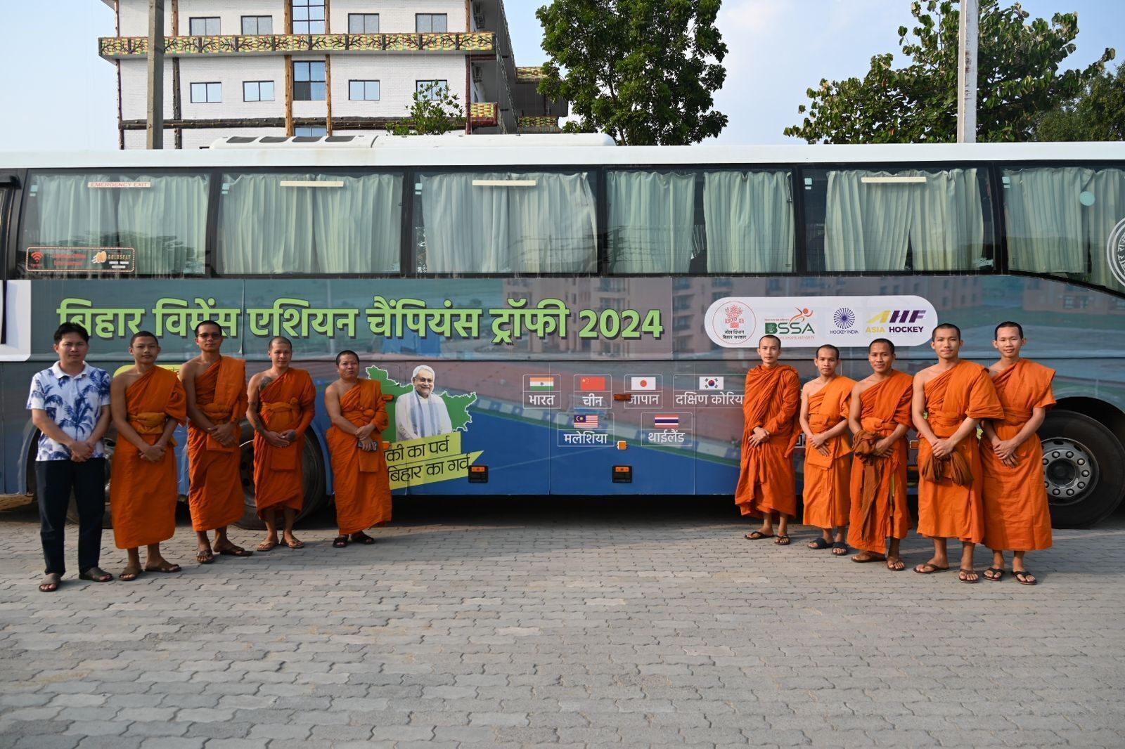 A group of monks standing in front of a bus with a banner displaying various country flags and logos.