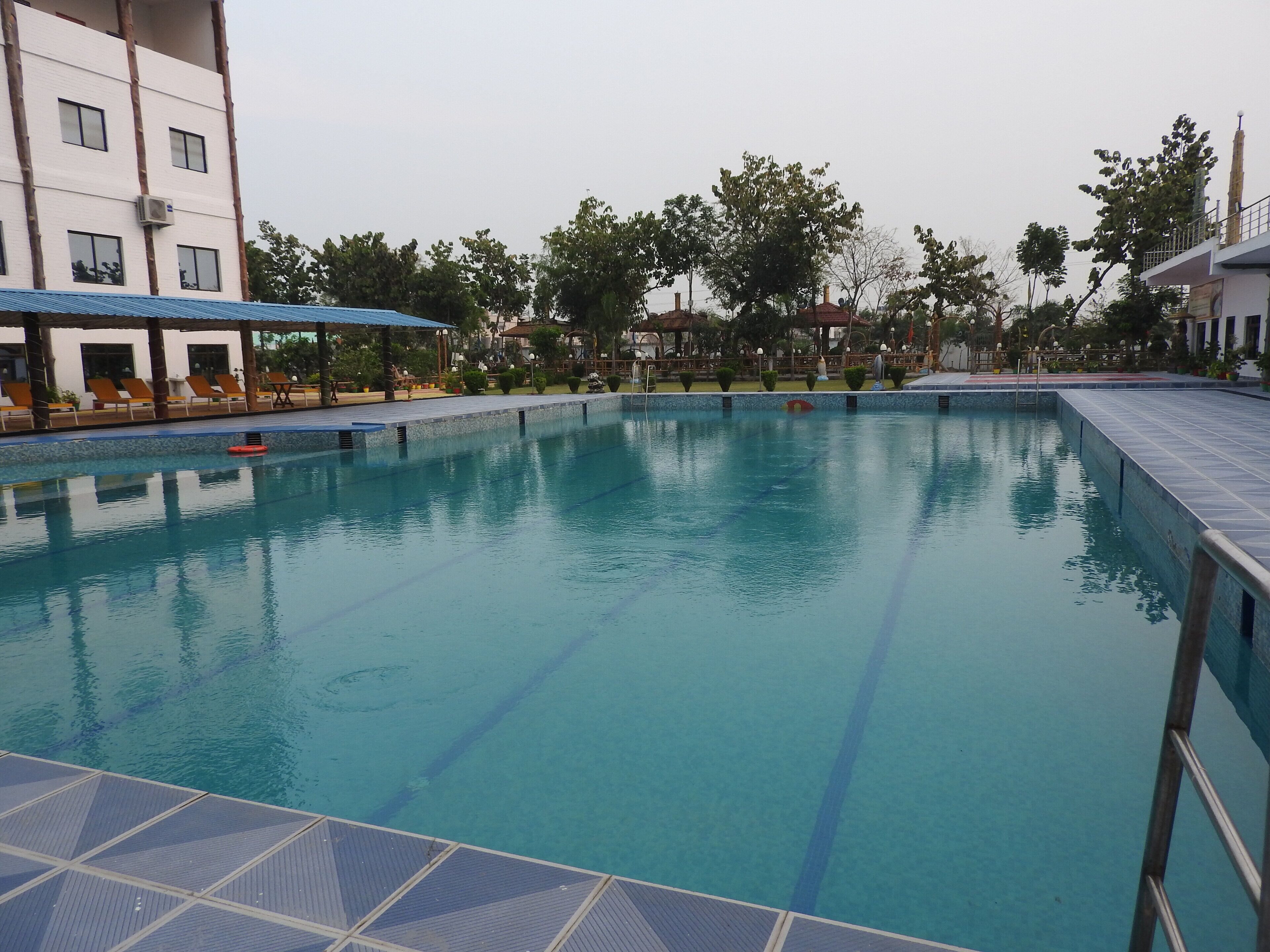 Una piscina con agua azul cristalina, rodeada de sillas de descanso y una zona de estar cubierta.