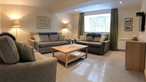 A cozy living room with two sofas, a coffee table, and two floor lamps. - Lategillan Cottage -  a cottage that sleeps 8 guests  in 3 bedrooms (Tweedsmuir)