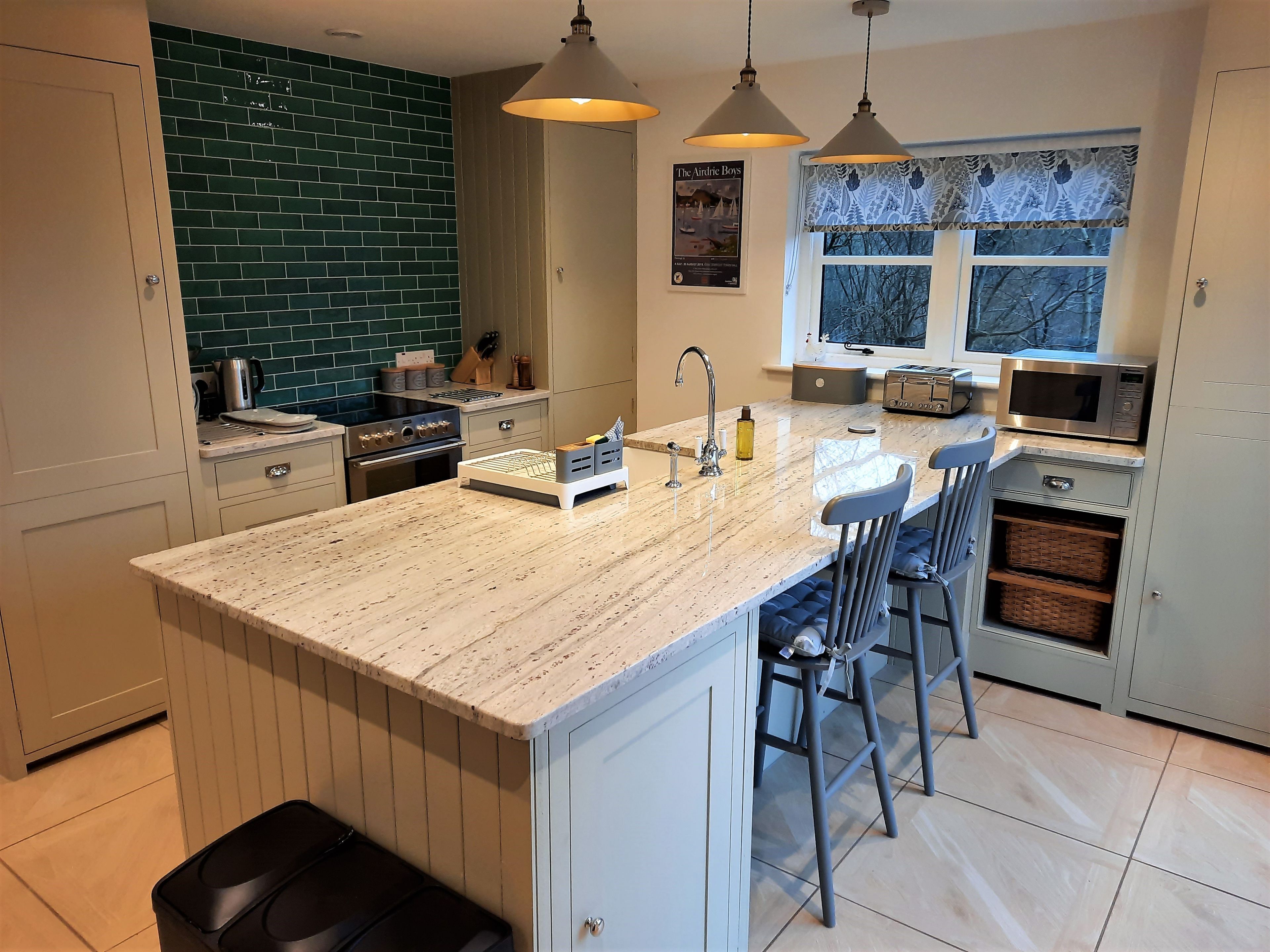 Una cocina moderna con una isla central, taburetes de bar, microondas y una ventana con cortinas estampadas.