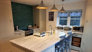 A modern kitchen with a central island, bar stools, a microwave, and a window with patterned curtains.