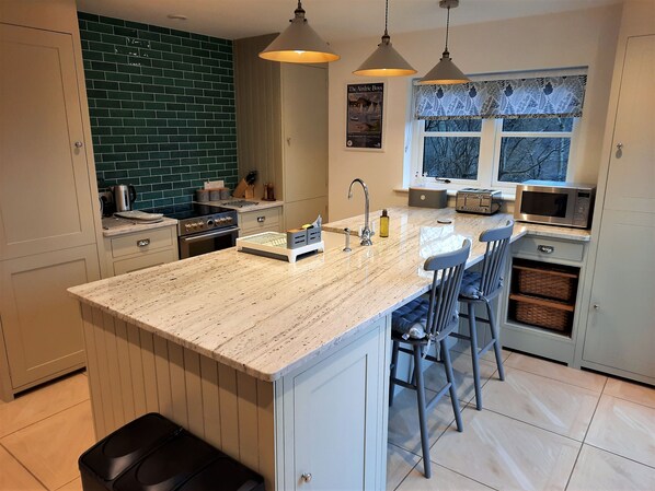 Cozinha moderna com ilha central, banquetas, micro-ondas e janela com cortinas estampadas.