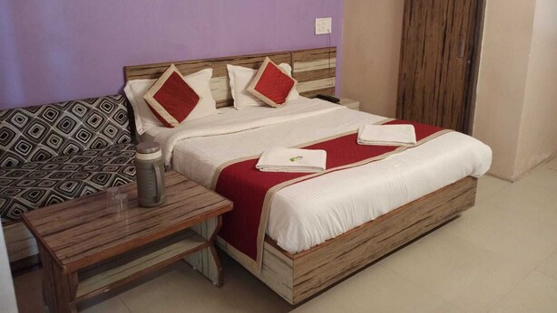 A neatly arranged bedroom with a bed, bedside table, and a patterned sofa. - Hotel Always Welcome (Abu Road)